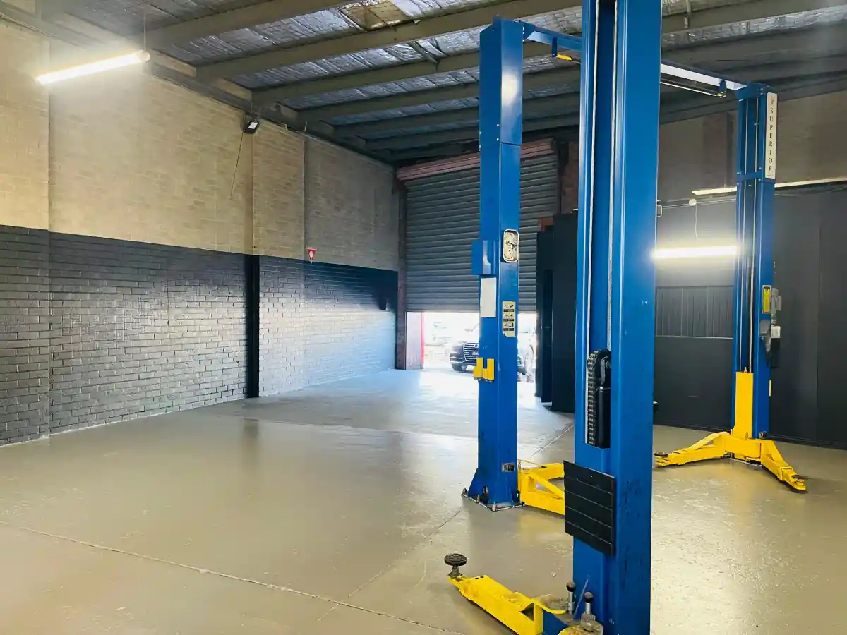 Empty service bay at AutoworkX with two-post hoists and a roller door open to the street