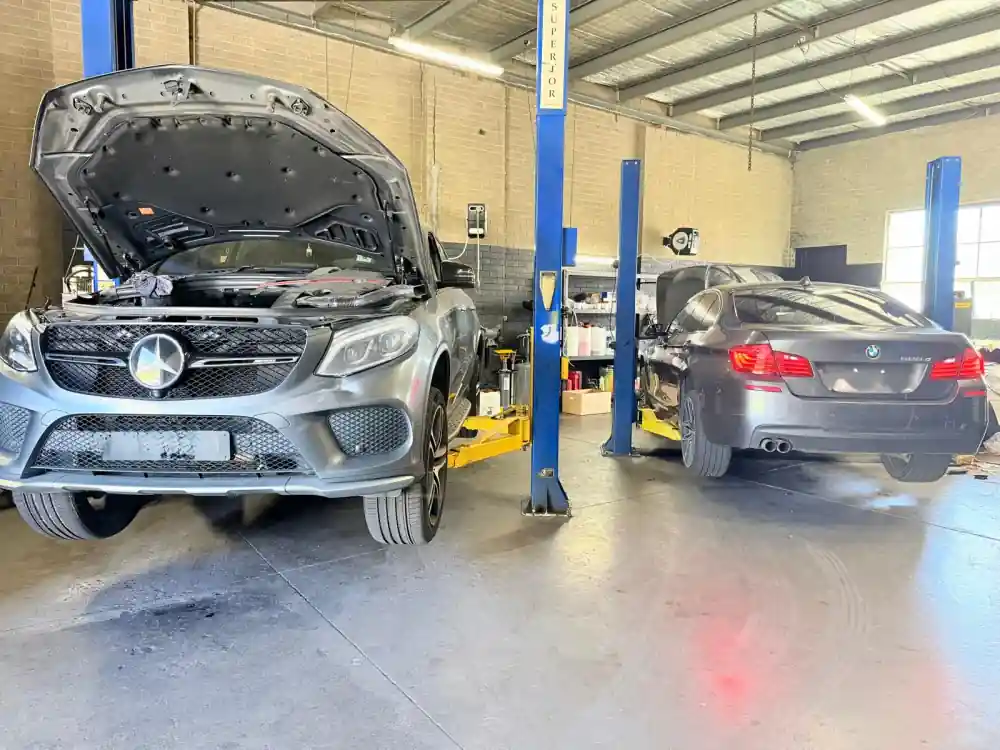 Mercedes-Benz GLE with the bonnet open on a hoist next to a BMW 5 Series under service