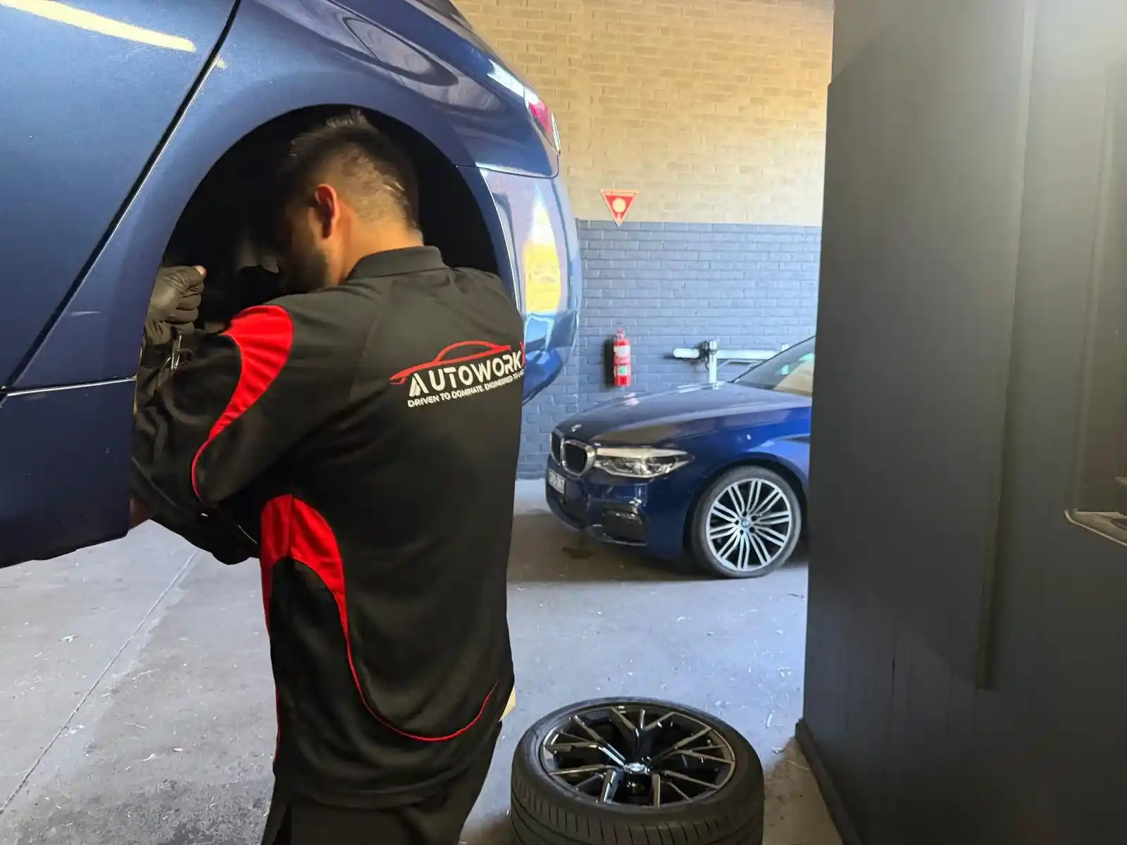 AutoworkX technician in a branded polo working inside the wheel arch of a BMW 5 Series