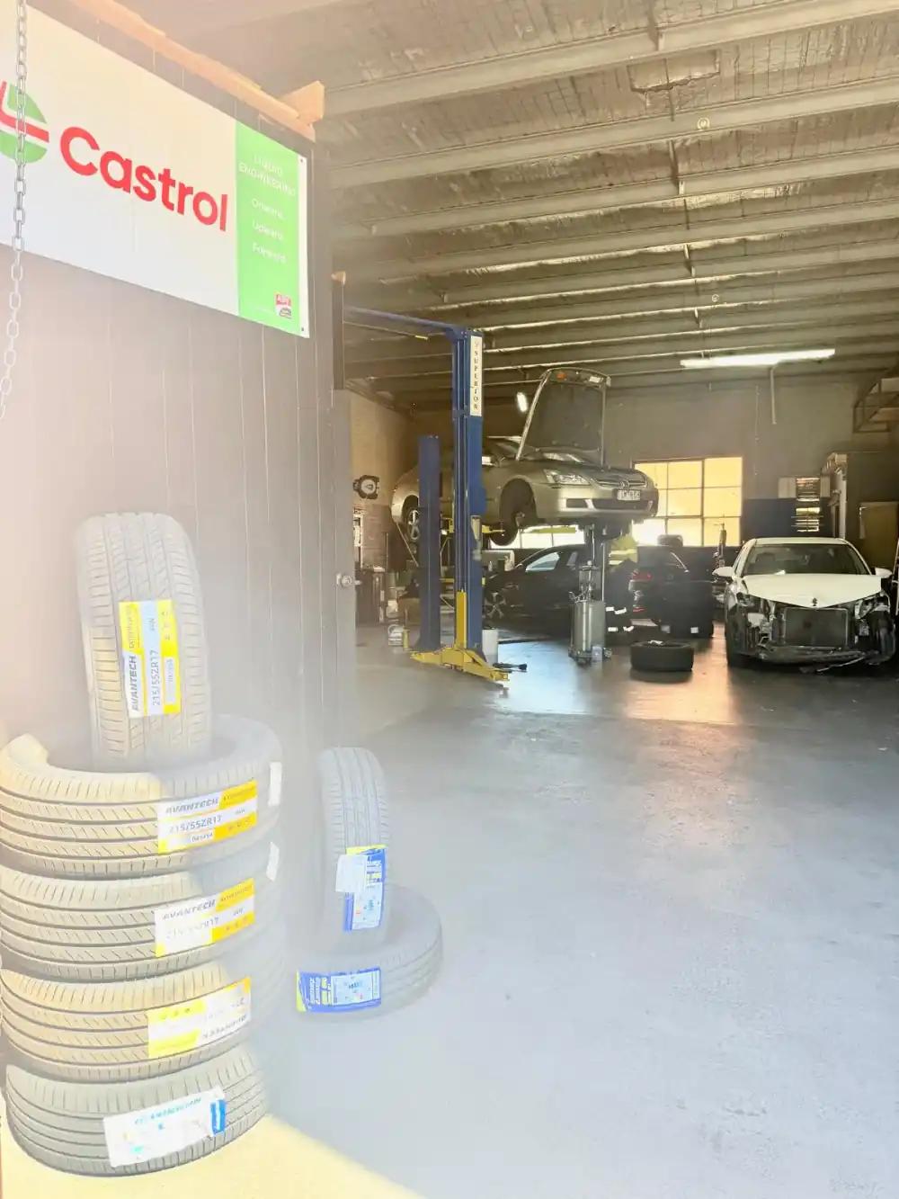 New tyres stacked beside the Castrol banner with the workshop floor beyond